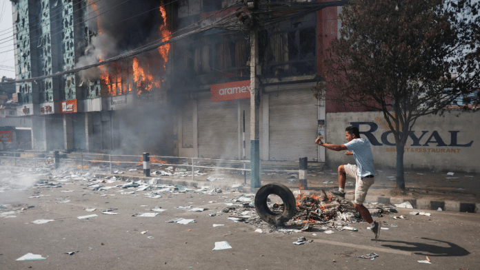 A pro-monarchist demonstrator kicks a tire next to a burning building during a protest demanding the restoration of Nepal's monarchy in Kathmandu | Reuters