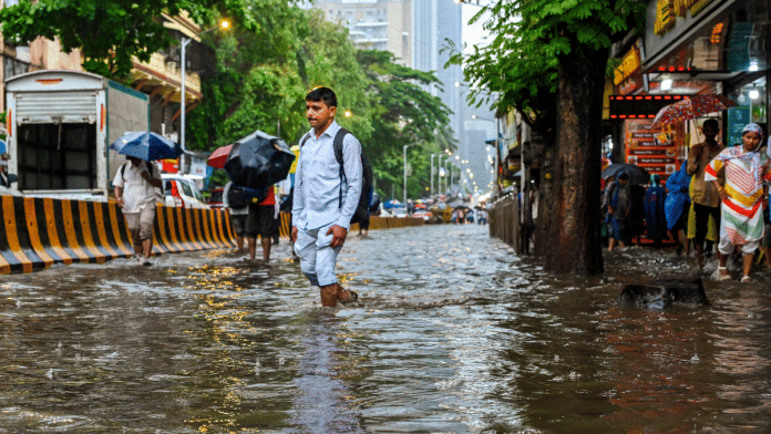People wade through a flooded road during rain, at Parel, in Mumbai, Monday | PTI
