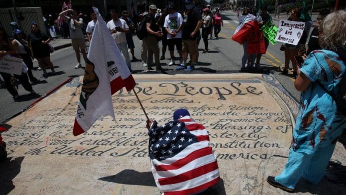 A man writes his name on a banner depicting the US Constitution during the No Kings protest against President Donald Trump's policies, in Los Angeles, California, on 14 June 2025 | Photo: Daniel Cole/Reuters