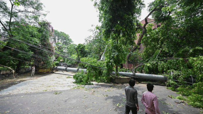 People walk past a 100-feet tall mobile tower that collapsed due to strong winds and rain, at Safdarjung Enclave, in New Delhi, on 15 June 2025. | PTI