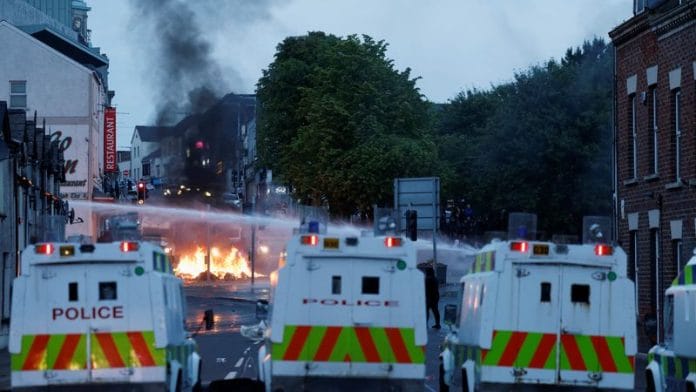 Official vehicles are parked as flames rise and a water cannon is used during a second night of riots, in Ballymena, Northern Ireland, on 10 June 2025. | Clodagh Kilcoyne | Reuters