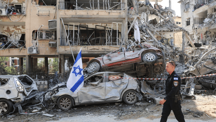 An Israeli police officer walks past damaged vehicles at an impact site following Iranian missile attack on Israel's Ramat Gan Saturday | Reuters/ANI
