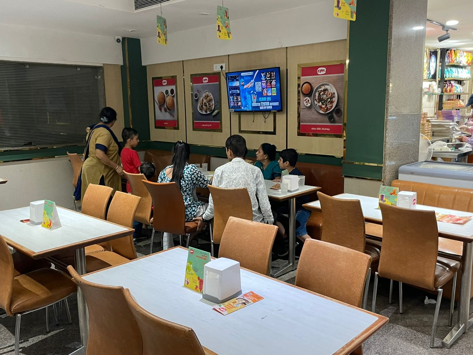 Interior of Om Sweets showing simple brown and white tables and modest dine-in setup.