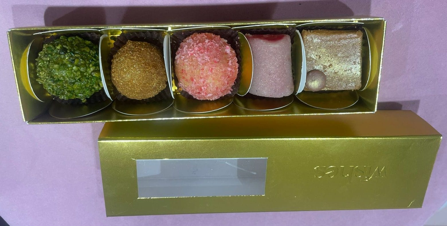 Display of handcrafted sweets at Wishes by Om, including pistachio, rose, and coconut ladoos.