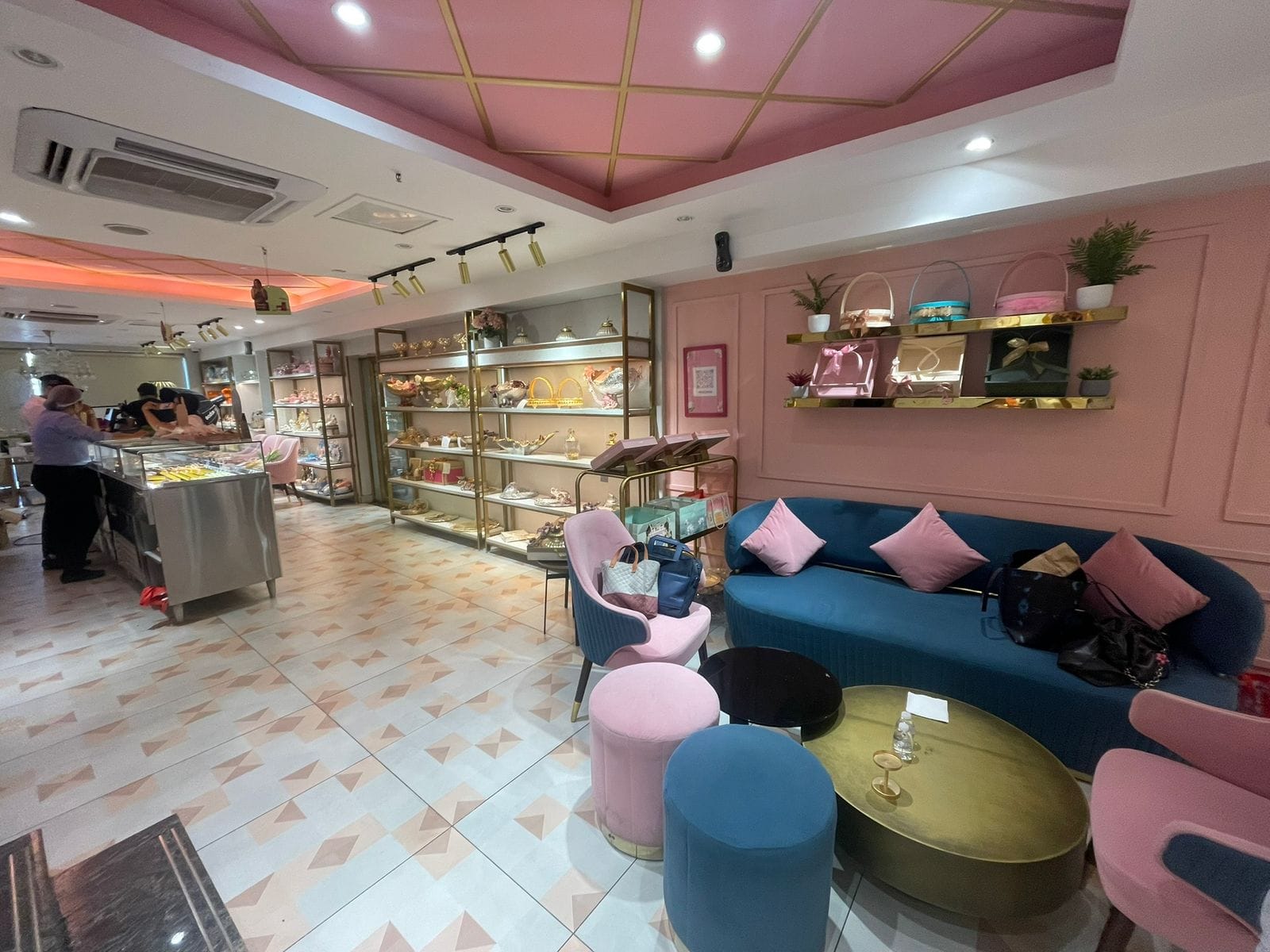 Chic interiors of Wishes by Om with pink and blue decor, plush seating, and runway-style mithai display.