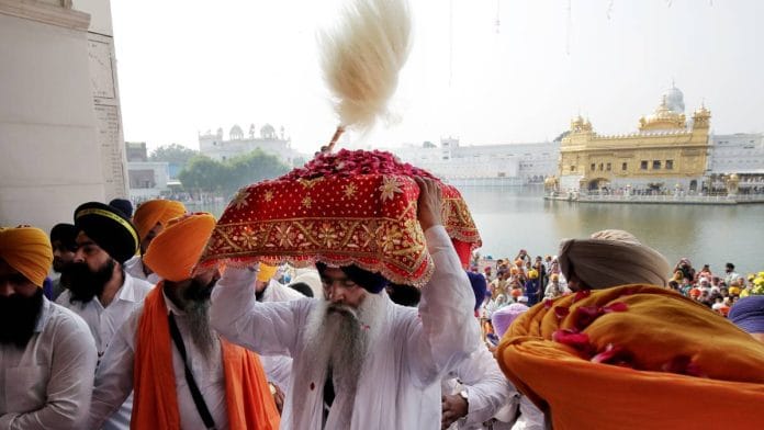 A Sikh priest carries the Guru Granth Sahib, holy book of the Sikhs, on his head during a religious procession at the Golden Temple in Amritsar | Photo: ANI