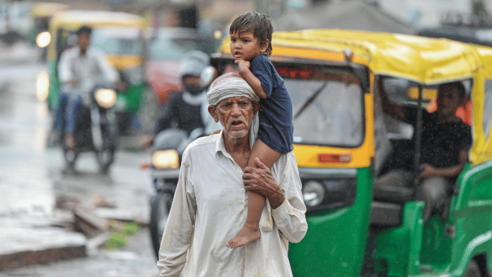 Representational image | A man with a boy on his shoulder walks on a busy road amid rain, in Bikaner on Saturday, 20 July 2025 | ANI