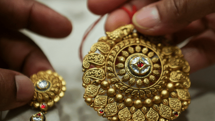 File photo of A woman holds a gold ornament at a jewellery shop in the old quarters of Delhi, India, May 24, 2023 | Reuters
