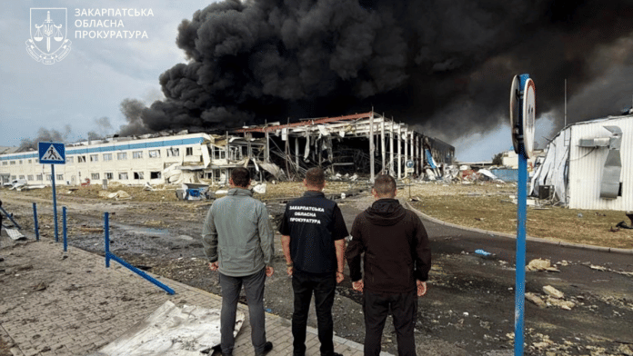 Law enforcement personnel watch as smoke rises over the Flextronics factory hit by a Russian missile strike, amid Russia's attack on Ukraine, in Mukachevo, Zakarpattia region, Ukraine August 21, 2025 | Zakarpattia Regional Prosecutor's Office/Handout via Reuters