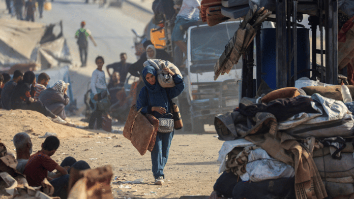 A displaced Palestinian woman, fleeing northern Gaza due to an Israeli military operation, walks with he belongings as she moves southward after Israeli forces ordered residents of Gaza City to evacuate to the south, on 22 September 2025. | Dawoud Abu Alkas | Reuters