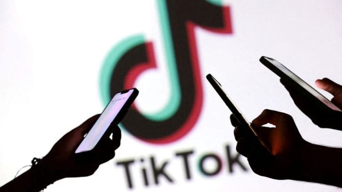 Teenagers pose for a photo while holding smartphones in front of a TikTok logo in this illustration taken on 11 September 2025. | Illustration | Dado Ruvic | Reuters