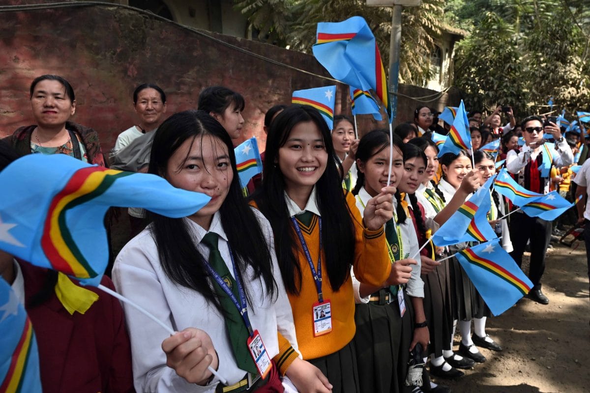 School students holding NSCN (IM) flags stand on the side of the road to welcome Muivah | ThePrint/Suraj Singh Bisht