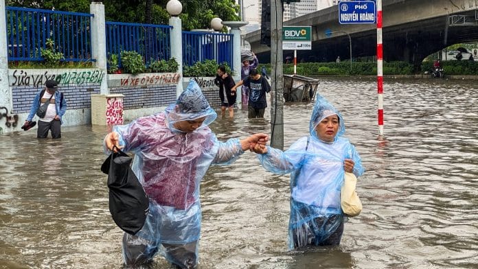 People wade through a flooded street amid heavy downpours from Typhoon Matmo, which stranded vehicles, closed schools in Hanoi on 7 October 2025. | Thinh Tien Nguyen | Reuters