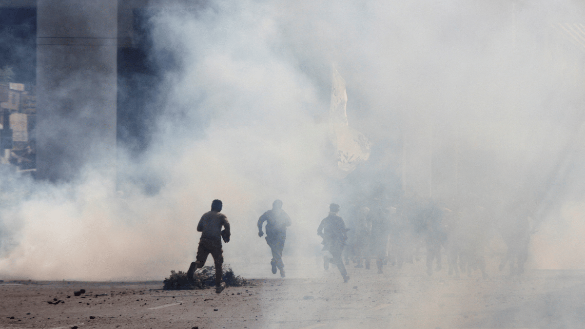 Police officers and supporters of TLP run amid tear gas fired by police during a solidarity march for Gaza in Lahore | Reuters