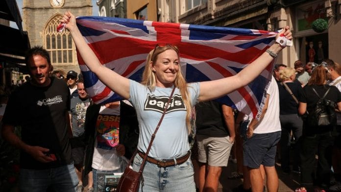 An Oasis fan holds up a Union Jack flag, ahead of the band's first show in 15 years, which is to take place at the Cardiff Principality Stadium, in Cardiff on 4 July 2025. | File Photo | Suzanne Plunkett | Reuters