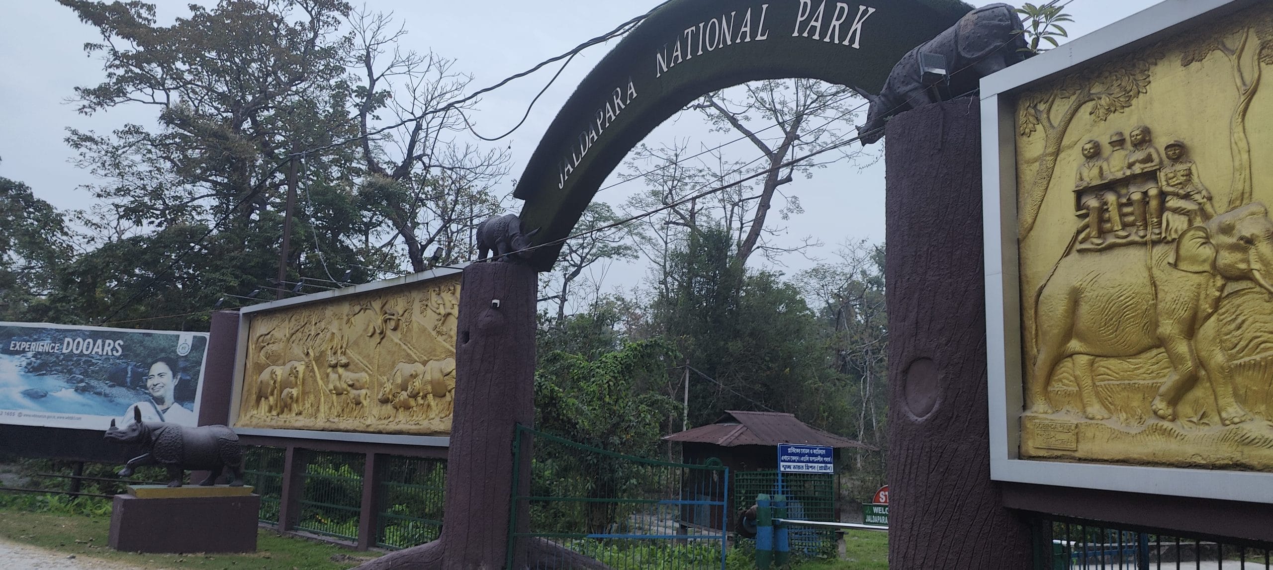 Gate of the Jaldapara National Park in north Bengal, which has become a safe haven for rhinos in the area. The gate is brown, has wood details and golden reliefs on both sides showing elephants and rhinos.