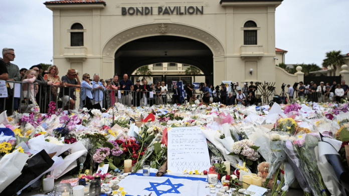 People stand near flowers laid as a tribute at Bondi Beach to honour the victims of a mass shooting that targeted a Hanukkah celebration at Bondi Beach on Sunday, in Sydney | Reuters