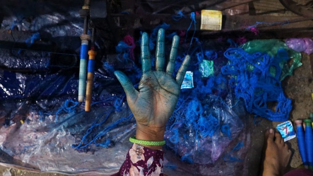 A woman shows her hand after dyeing a thread in blue. Manisha Mondal | ThePrint