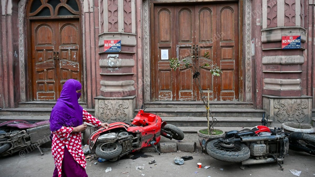 A woman walks past two-wheelers damaged in the chaos during midnight demolition drive on 7 January 2026 | Suraj Singh Bisht/ThePrint
