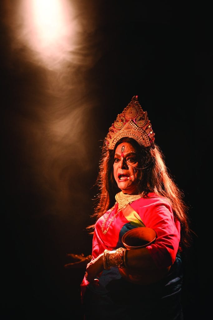 Chapal Bhaduri wearing a crown, with a third eye painted on the forehead, carrying an earthen pot with dramatic lighting.