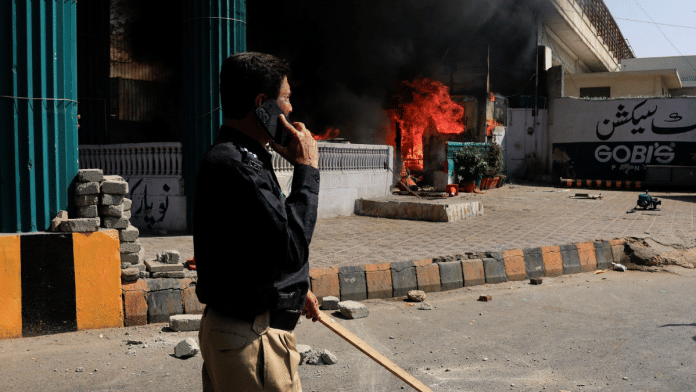 A police officer walks next to a checkpost set ablaze in a protest outside the U.S. Consulate General in Karachi on Sunday | REUTERS/Akhtar Soomro 
