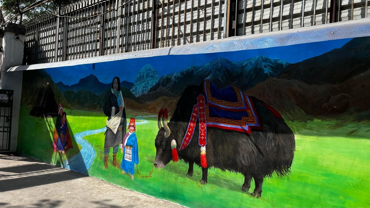 The mural at the entrance of Samyeling Gate No. 2 shows a traditional Tibetan family wearing chubas 