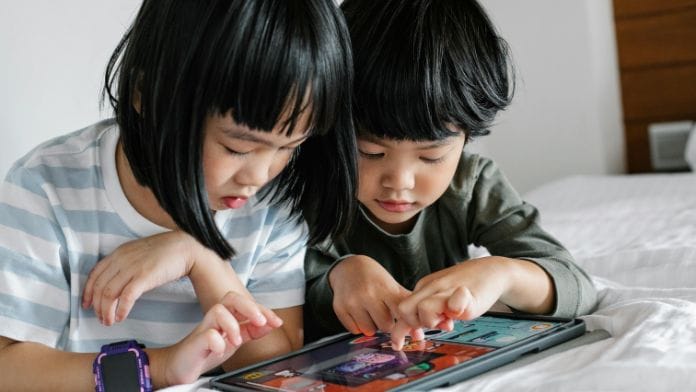 Two children peering into a large screen, playing a video game