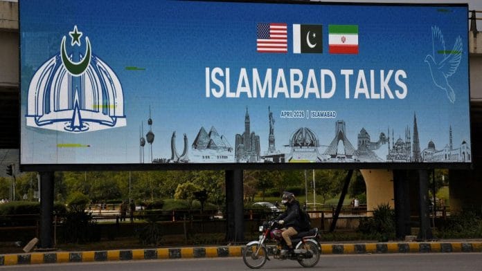 A man rides his motorbike past a billboard as Pakistan prepares to host US and Iran for peace talks, in Islamabad | Photo: Reuters/Waseem Khan