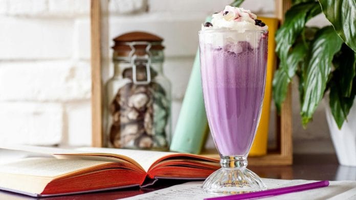 A tall glass of a purple drink topped with white ice cream.
