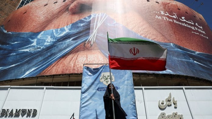 A woman holds an Iranian flag near an anti-U.S. billboard depicting U.S. President Donald Trump and the Strait of Hormuz, in Tehran, Iran, May 25, 2026. | Majid Asgaripour/WANA (West Asia News Agency) via REUTERS