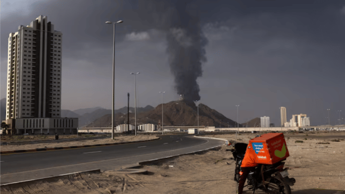 Representational | A person stands next to a motorcycle as smoke rises in the UAE's Fujairah oil industry zone following a fire caused by debris after interception of a drone by air defenses | Reuters
