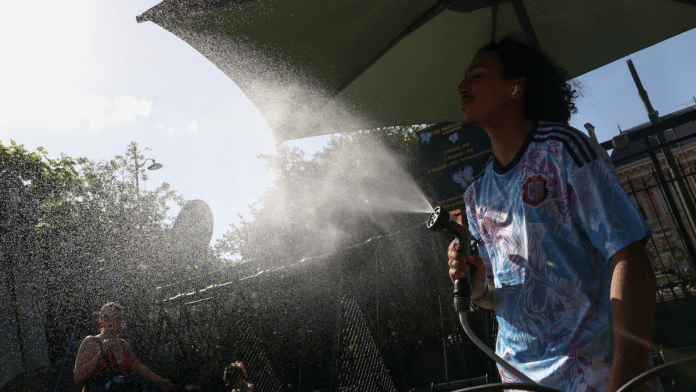 A worker sprays water on people passing by in Buttes Chaumont park, as temperatures reached up to 35 degrees Celsius, during a period of hot weather in Paris, France | REUTERS/Tom Nicholson