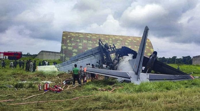 Security personnel and others stand near damaged remains of a transport aircraft of the Indian Air Force that crashed while landing, in Jorhat district, Assam. | @AjayTamtaBJP /X via PTI Photo