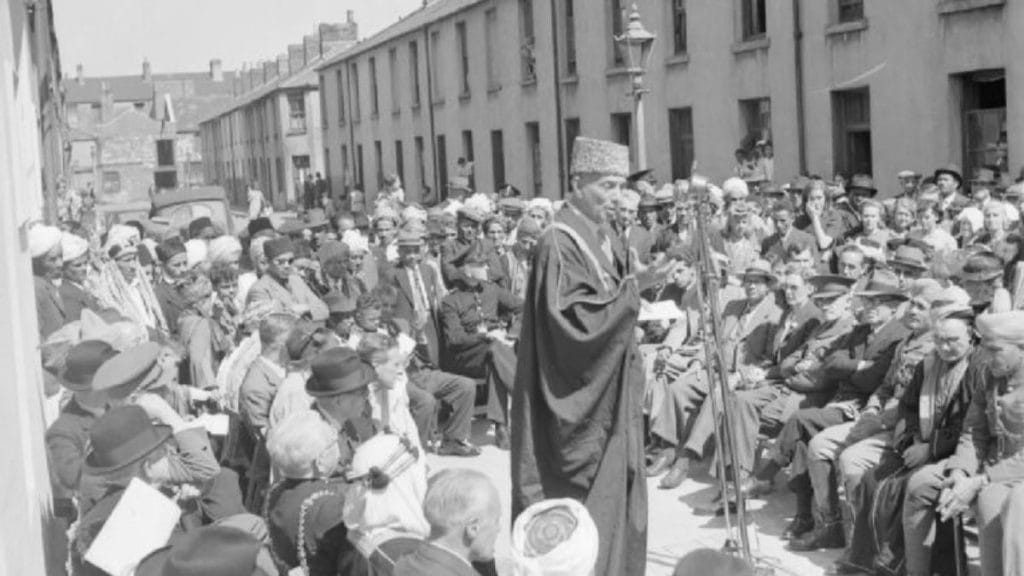 Hassan Suhrawardy stands at a microphone as he speaks to the audience in Cardiff. Image: Wikipedia