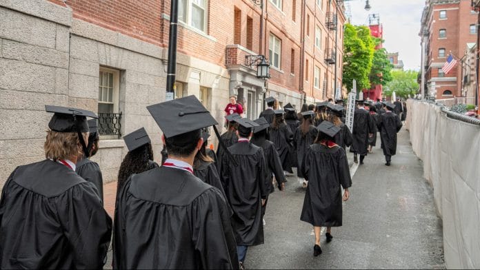 University students wearing graduation gowns walk in Cambridge, Massachusetts. | Bloomberg