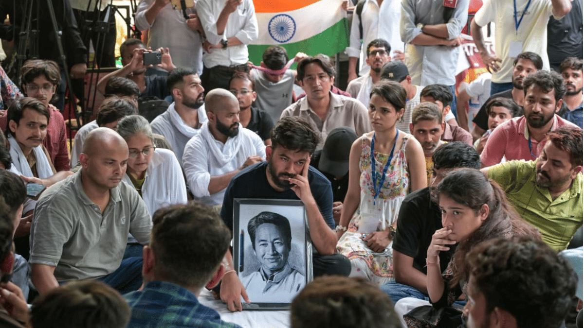 Cockroach Janta Party leader Abhijit Dipke sitting with a photograph of Wanghchuk at Jantar Mantar protest site | Suraj Singh Bisht | ThePrint