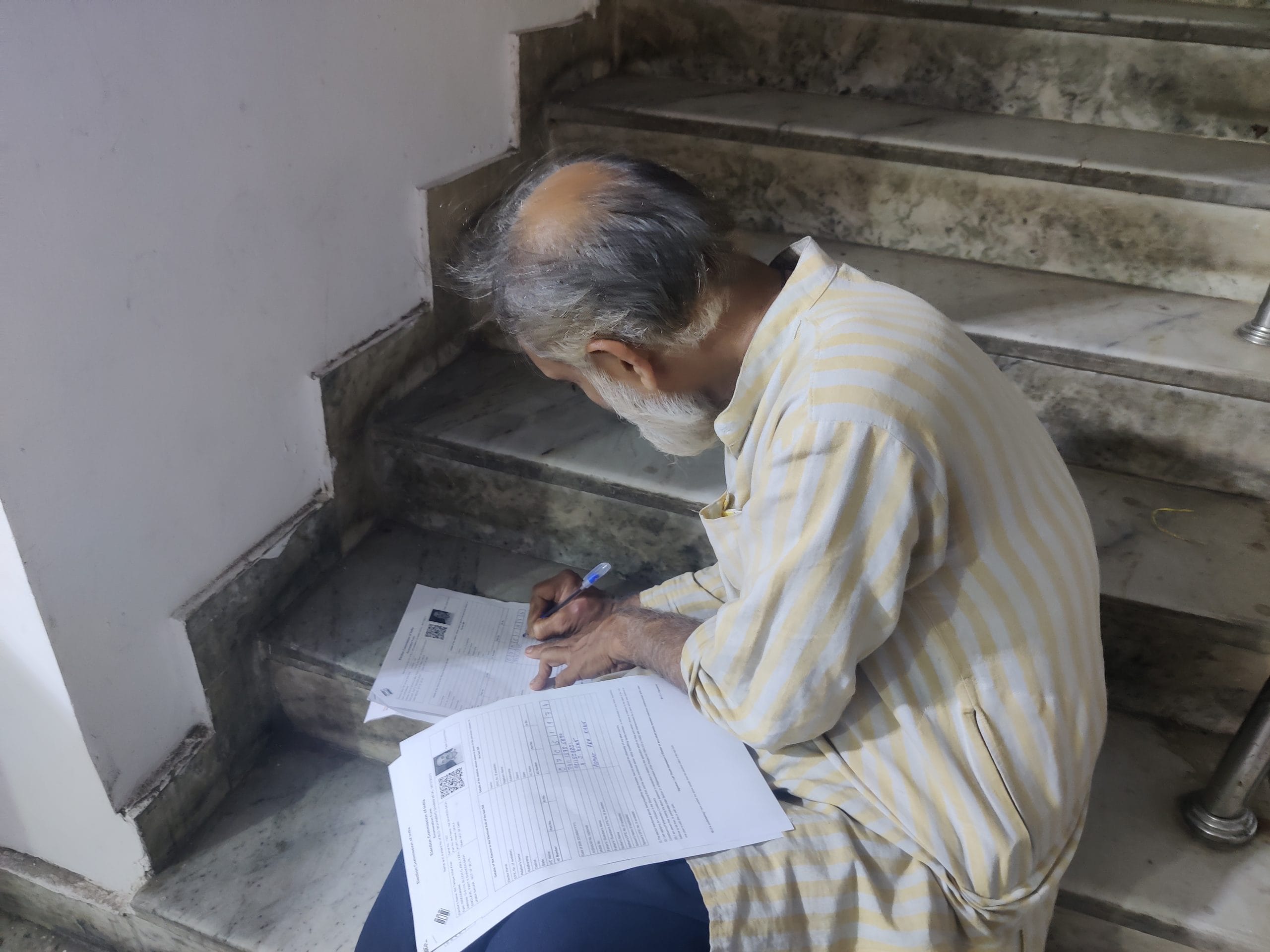 Fifty-three-year-old Tariq Khan sits on a corner of the school staircase. He had expected the process to be easy, especially because his father was a government officer, but what he thought would be a straightforward task turned into an unexpected challenge. (Photo: Almina Khatoon | The Print)