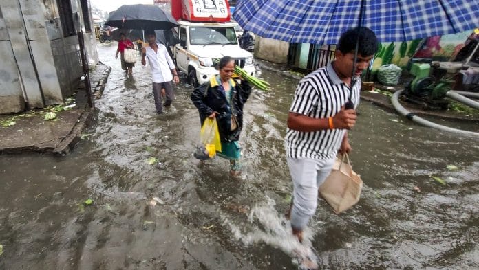 Pedestrians make their way through a waterlogged road amid rainfall, in Navi Mumbai, Maharashtra | PTI Photo
