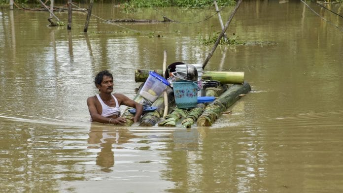 A man carrying his belongings on a makeshift raft wades through a waterlogged area after floods and heavy rain, in Sivasagar, Assam | PTI