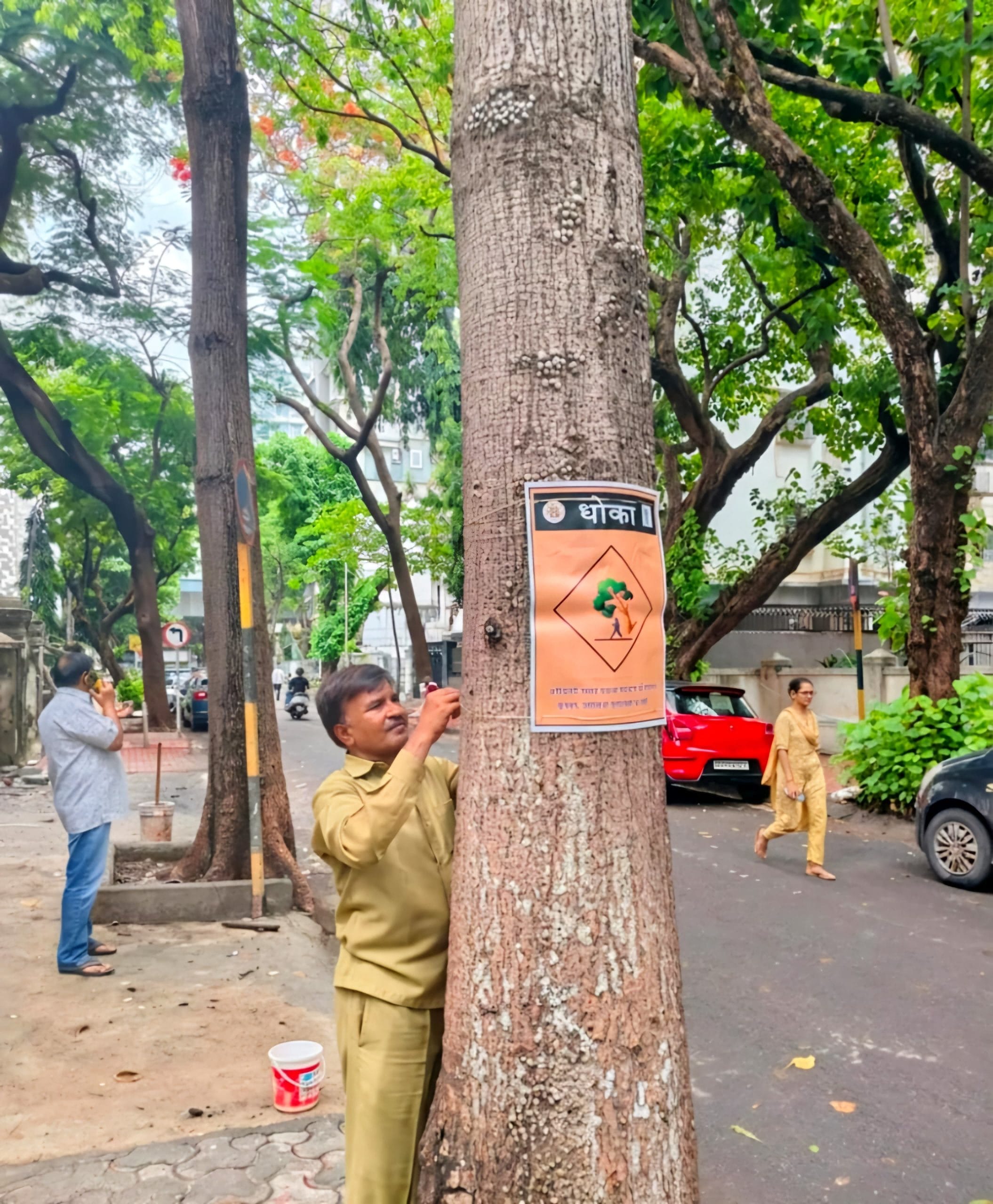 A municipal worker puts up a hazard warning notice on a tree marked "Dhoka" (Danger), cautioning people against standing or parking beneath it | Photo by special arrangement