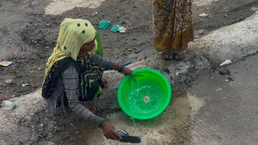 A woman collects pooled rainwater from an elevated highway stretch, using her slipper to splash the water into a plastic bucket. Saman Husain | ThePrint