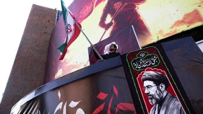 A man holding an Iranian flag, next to a picture of Iran's Supreme Leader Mojtaba Khamenei, in Tehran on 13 August, 2026 | Majid Asgaripour/WANA via Reuters
