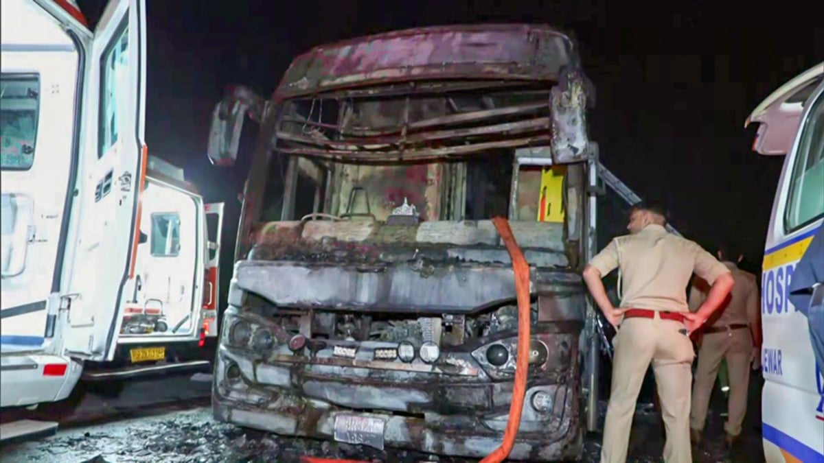A police official standing next to the charred sleeper bus that caught fire | ANI
