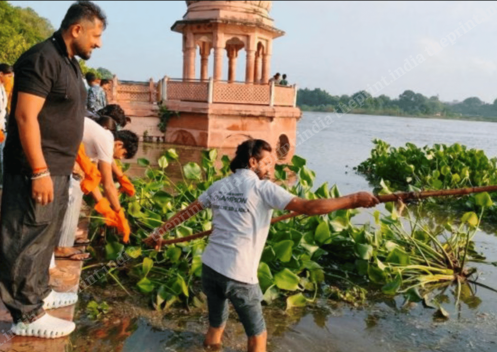Radio jockey Prateek Bharadwaj (in black) watches as Akash, a sales executive, clears vegetation from the Gomti with a long rake as part of the Go For Gomti volunteer drive in Lucknow | Harsh Tiwari/ThePrint
