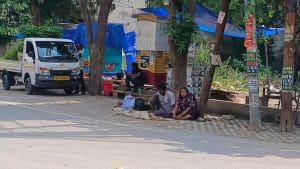 अनुज, उनकी पत्नी लता और उनके पिता गोपाल सिंह गेट के सामने प्रोटेस्ट करते हुए तेज धूप से बचने के लिए एक पेड़ की छांव में बैठे हैं | फोटो: अलमिना खातून/दिप्रिंट
