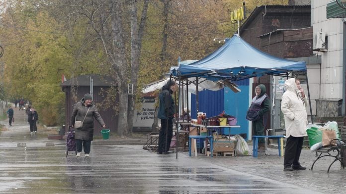 A woman carrying a bucket pulls a cart past a street market in the town of Shelekhov in the Irkutsk region, Russia, October 6, 2026, in this still image taken from video. REUTERS/Stringer