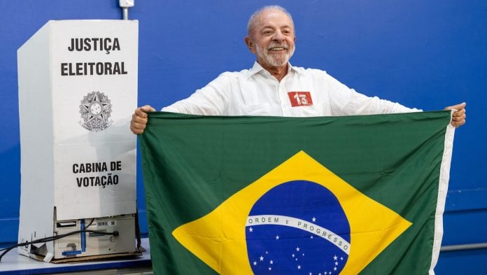 Lula holds a Brazilian national flag at a polling station during the runoff election in Sao Bernardo do Campo on Oct. 25 | Bloomberg
