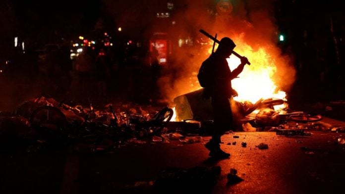 A person walks as flames rise during civil unrest, the day after a national day of demonstrations against the cost of living and rising fuel prices, in Paris, France, October 18, 2026. REUTERS/Abdul Saboor