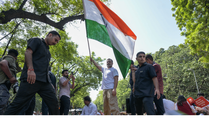 Lok Sabha LoP Rahul Gandhi holds the tricolour while standing on a barricade near Akashvani Bhawan during INDIA bloc's protest march from Parliament House to EC office | Suraj Singh Bisht | ThePrint